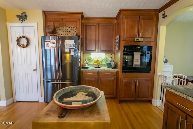 kitchen with arched walkways, black oven, light wood finished floors, and freestanding refrigerator