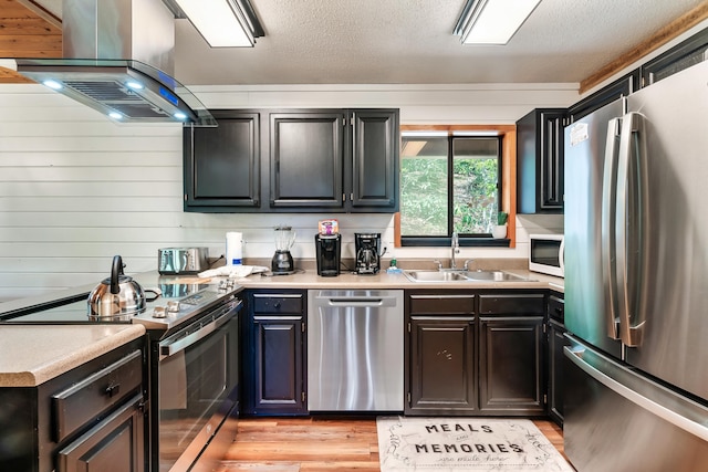 kitchen featuring a textured ceiling, a sink, appliances with stainless steel finishes, light wood finished floors, and island exhaust hood