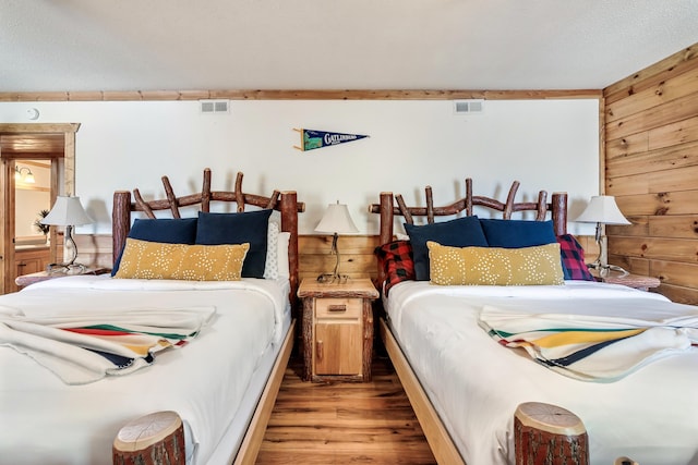 bedroom featuring visible vents, wood walls, and wood finished floors