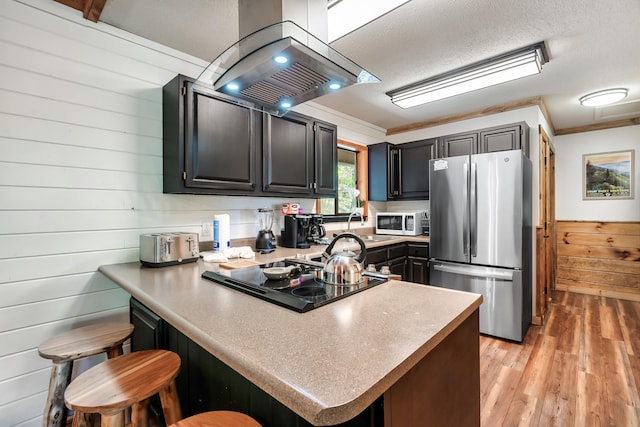 kitchen featuring island range hood, a breakfast bar area, freestanding refrigerator, a peninsula, and black electric cooktop