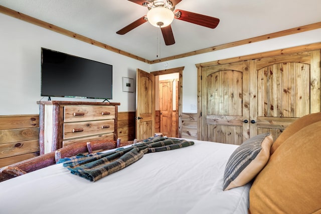 bedroom featuring a ceiling fan, a wainscoted wall, and wooden walls