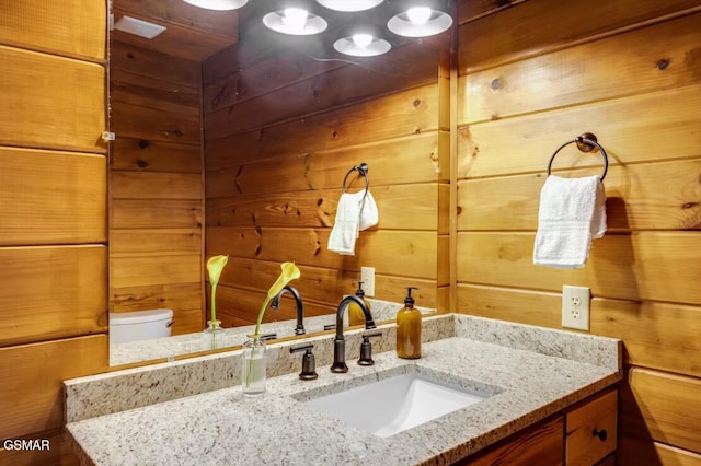 bathroom featuring toilet, wood walls, and vanity