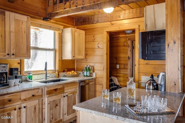 kitchen with light stone counters, light brown cabinets, wood walls, a sink, and dishwasher