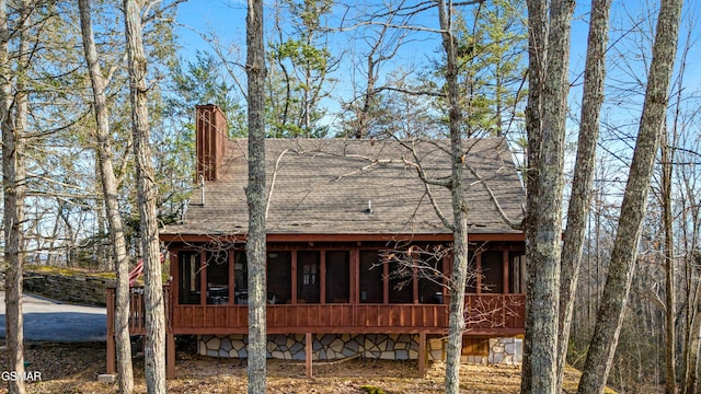 back of house featuring a sunroom, a shingled roof, and a chimney