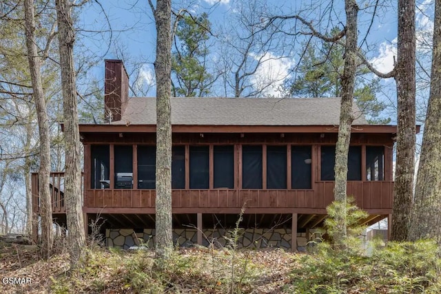 back of house featuring a shingled roof, stone siding, and a chimney