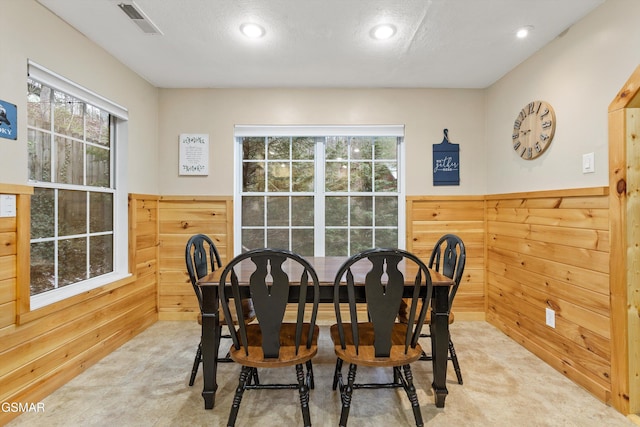 dining room with wood walls, wainscoting, visible vents, and a healthy amount of sunlight