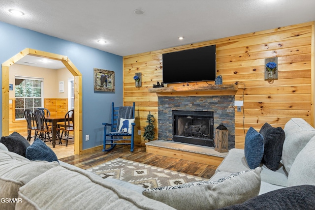 living area with arched walkways, recessed lighting, wooden walls, a fireplace, and wood finished floors