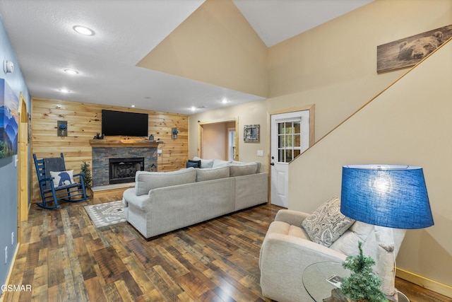 living area with a stone fireplace, dark wood-type flooring, recessed lighting, and wooden walls