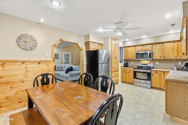 kitchen with arched walkways, stainless steel appliances, tasteful backsplash, a ceiling fan, and a sink