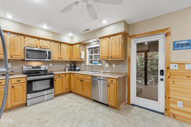 kitchen with stainless steel appliances, a sink, a ceiling fan, light countertops, and decorative backsplash