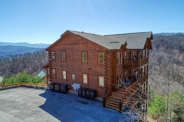 rear view of house featuring log exterior, a patio, and a wooded view