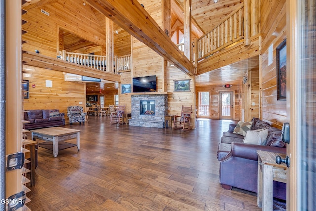 living area featuring a stone fireplace, wooden walls, wood finished floors, and a high ceiling