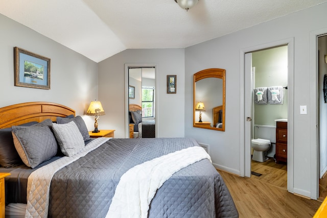 bedroom with a textured ceiling, ensuite bathroom, light hardwood / wood-style flooring, and lofted ceiling