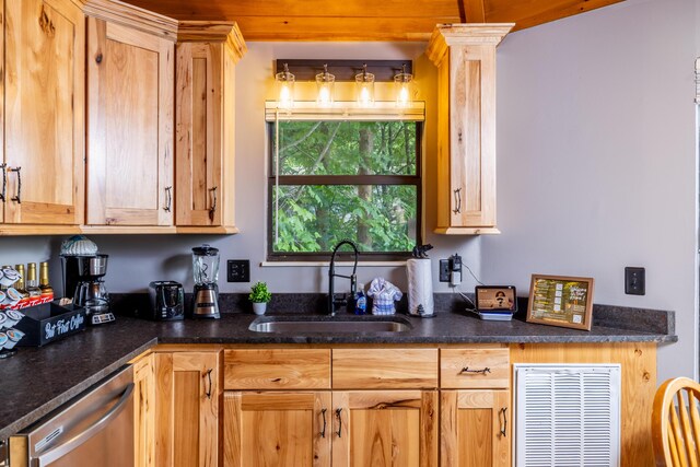 kitchen featuring ornate columns, stainless steel dishwasher, dark stone counters, and sink