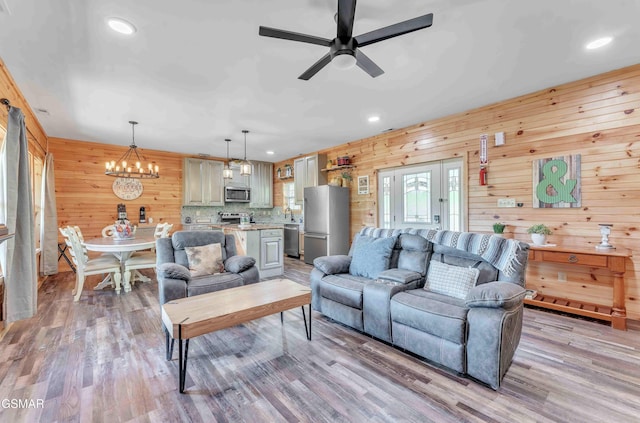 living area featuring wooden walls, light wood-type flooring, recessed lighting, and ceiling fan with notable chandelier