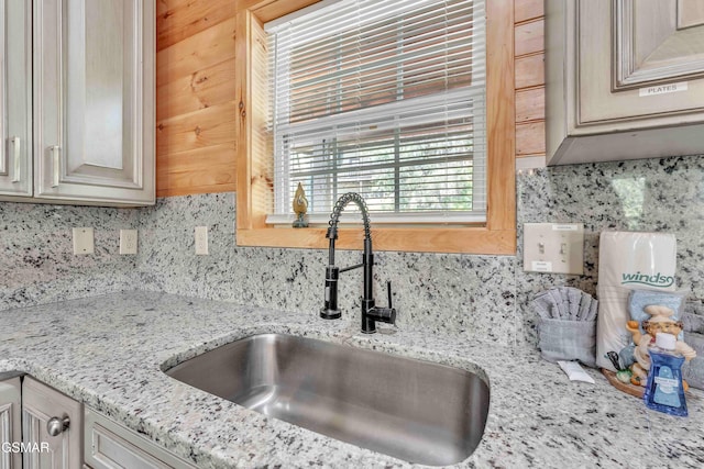 kitchen with light stone countertops, a sink, and backsplash