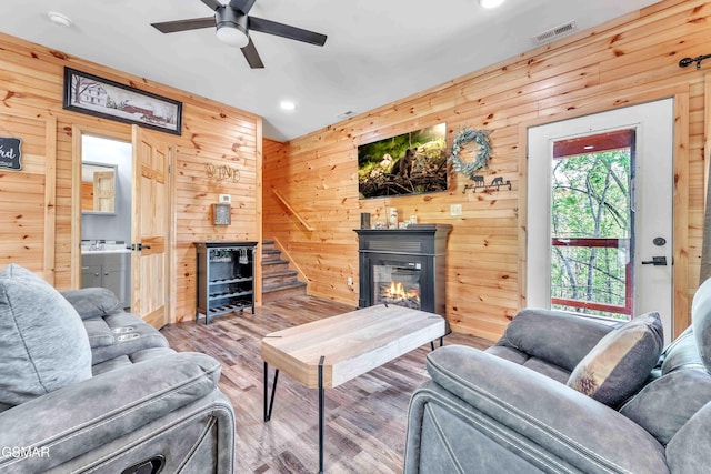 living room with visible vents, a ceiling fan, wooden walls, recessed lighting, and a glass covered fireplace