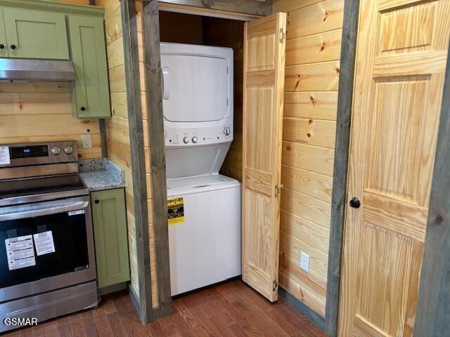 laundry room with stacked washer and dryer, dark hardwood / wood-style floors, and wood walls