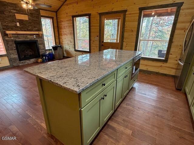 kitchen with dark hardwood / wood-style flooring, wood walls, vaulted ceiling, a fireplace, and a kitchen island