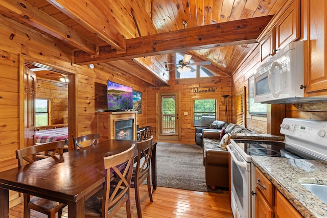 dining space featuring wooden walls, a ceiling fan, a tiled fireplace, wood ceiling, and light wood-style floors