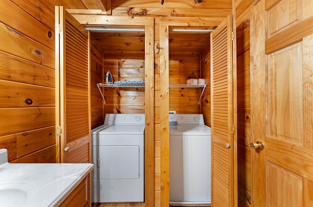 clothes washing area featuring laundry area, wood walls, and separate washer and dryer