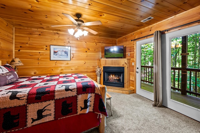 carpeted bedroom featuring wooden walls, access to outside, ceiling fan, and wooden ceiling