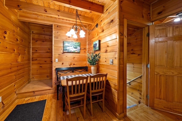 dining area featuring wood walls, wooden ceiling, beamed ceiling, a notable chandelier, and wood-type flooring