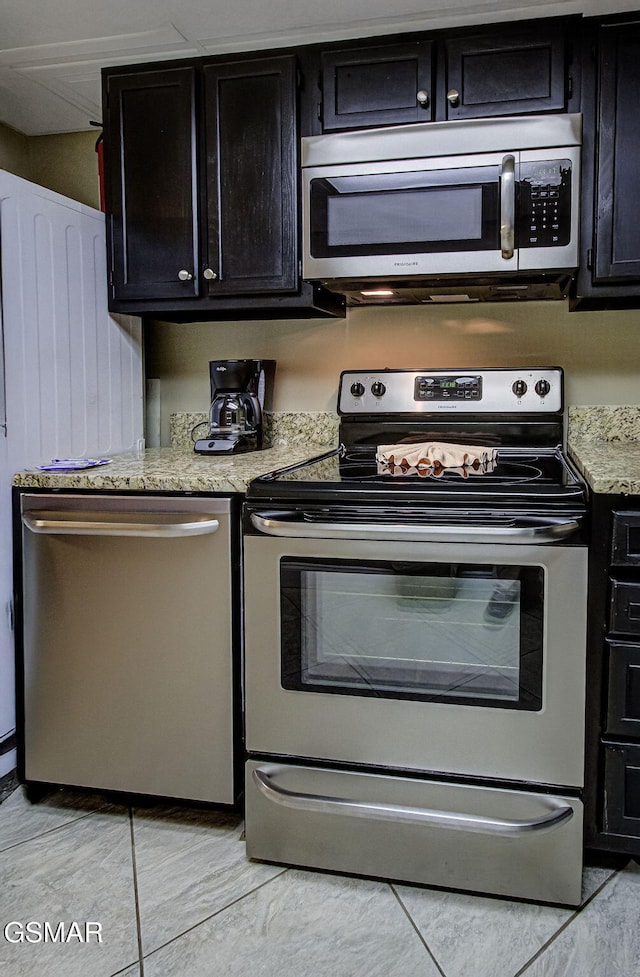 3215 N River Rd Unit 103, Pigeon Forge, TN 37863 - kitchen featuring appliances with stainless steel finishes, dark cabinets, light tile patterned floors, and light stone countertops