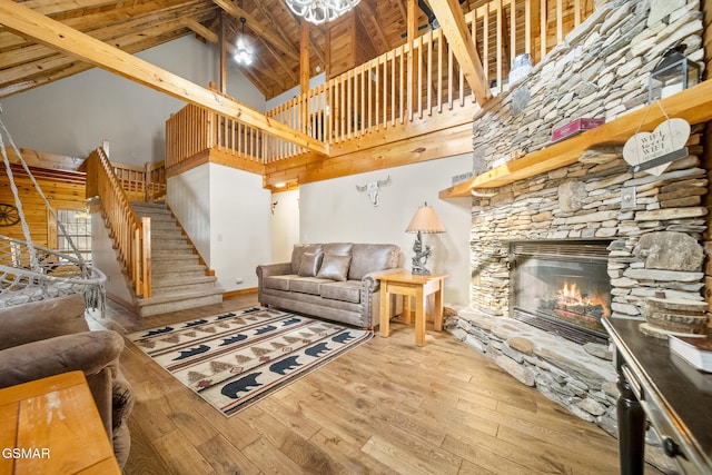 living room with a stone fireplace, wood finished floors, wooden ceiling, beamed ceiling, and stairs