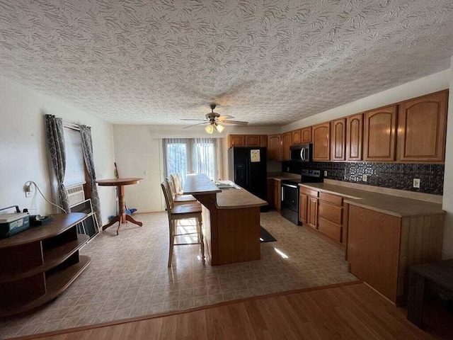 kitchen featuring ceiling fan, a center island, a kitchen breakfast bar, appliances with stainless steel finishes, and light wood-type flooring