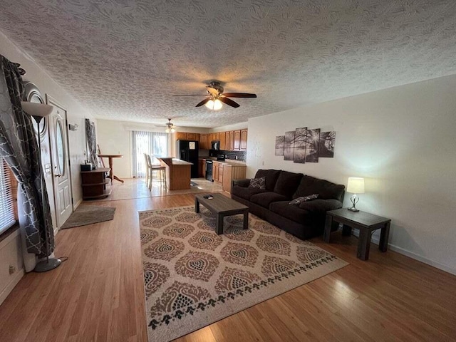 living room with ceiling fan, light hardwood / wood-style flooring, and a textured ceiling