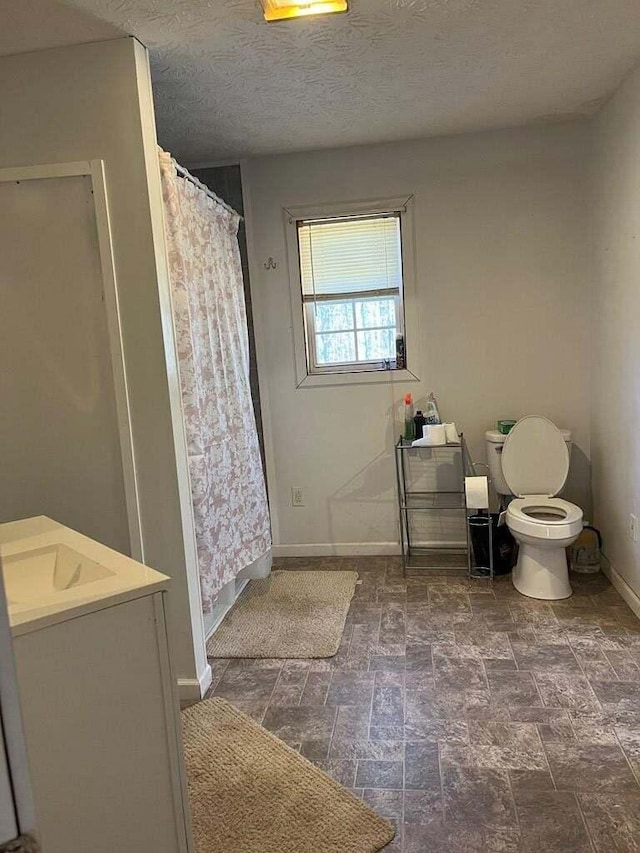 bathroom with a textured ceiling, vanity, toilet, and curtained shower