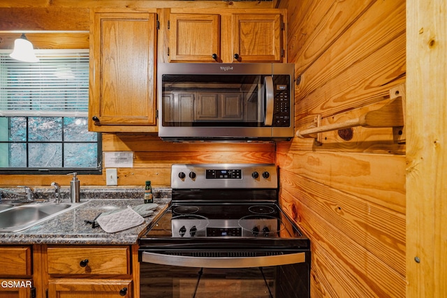 kitchen featuring wood walls, sink, dark stone counters, and appliances with stainless steel finishes