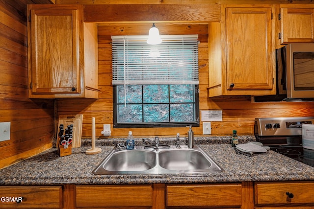 kitchen with dark stone countertops, stainless steel appliances, wooden walls, and sink