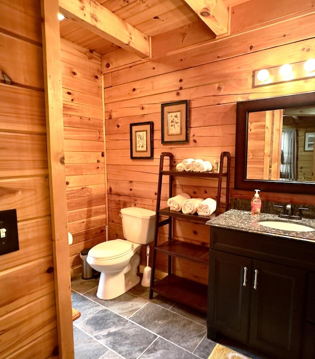 bathroom with wooden ceiling, beamed ceiling, wood walls, toilet, and vanity