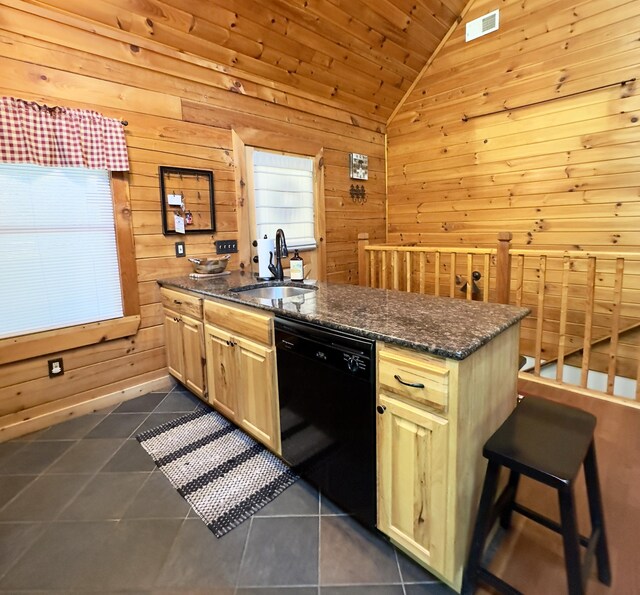 kitchen featuring sink, dark tile patterned flooring, dark stone countertops, black dishwasher, and wood walls