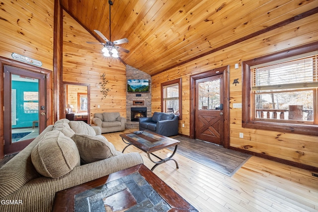 living room featuring a stone fireplace, wooden ceiling, wood walls, light wood-type flooring, and ceiling fan