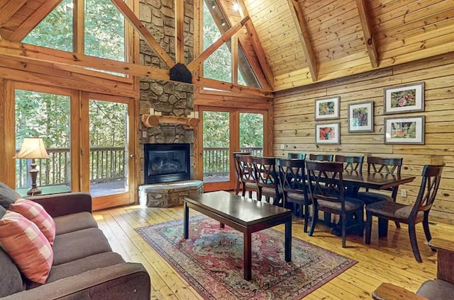 living room featuring wood walls, wooden ceiling, high vaulted ceiling, a stone fireplace, and beamed ceiling