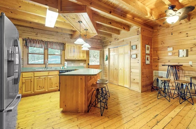 kitchen with stainless steel refrigerator with ice dispenser, ceiling fan, sink, a center island, and wood walls