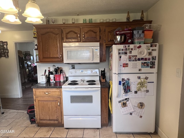 kitchen with dark countertops, light tile patterned floors, white appliances, and baseboards