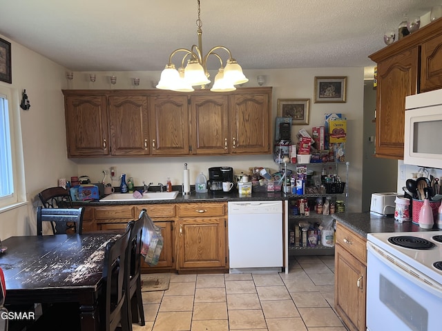 kitchen with white appliances, light tile patterned floors, an inviting chandelier, dark countertops, and brown cabinets