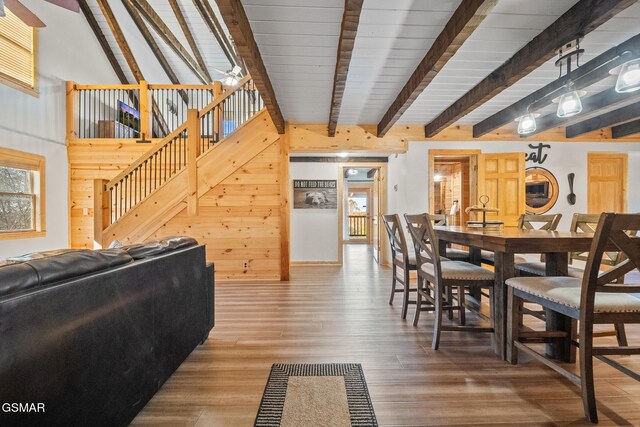 dining space with ceiling fan, lofted ceiling with beams, wood-type flooring, and wooden walls