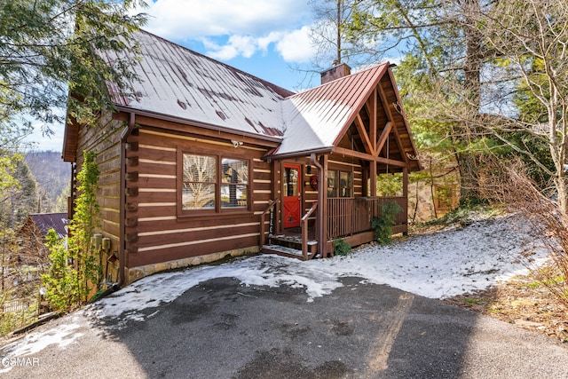 cabin with metal roof, a porch, log siding, a standing seam roof, and a chimney