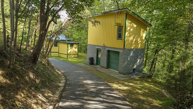 view of side of home featuring an outbuilding, stone siding, and driveway