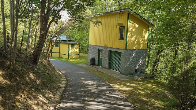 view of home's exterior with an outbuilding, stone siding, and driveway