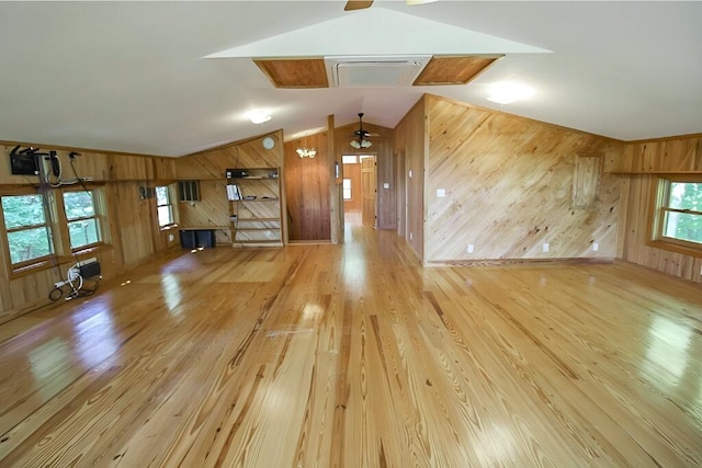 unfurnished living room featuring lofted ceiling, wooden walls, and wood finished floors