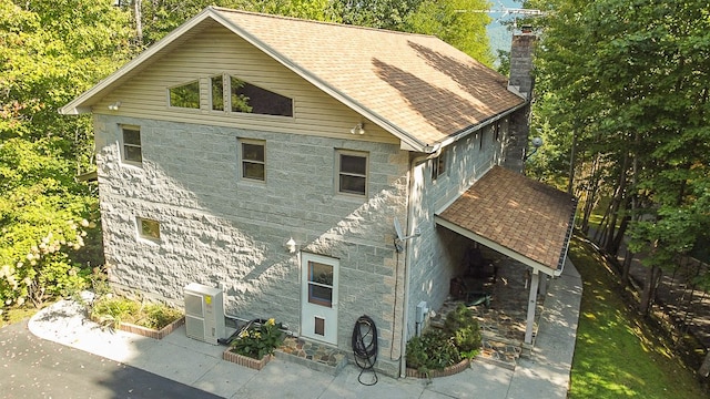 exterior space featuring stone siding, a shingled roof, and a chimney