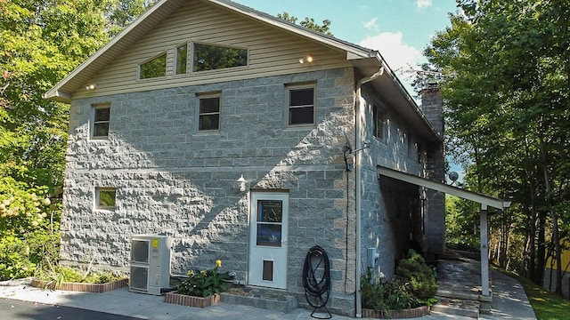 exterior space with central air condition unit, stone siding, and a chimney