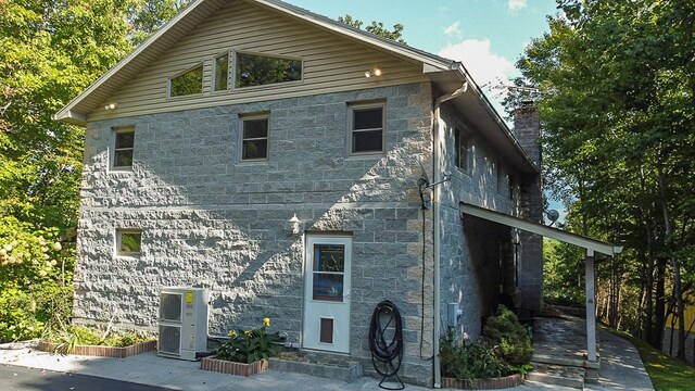 exterior space featuring stone siding, a chimney, and central air condition unit