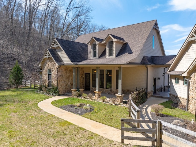 view of front of house featuring a shingled roof, fence, a front yard, stone siding, and a gate